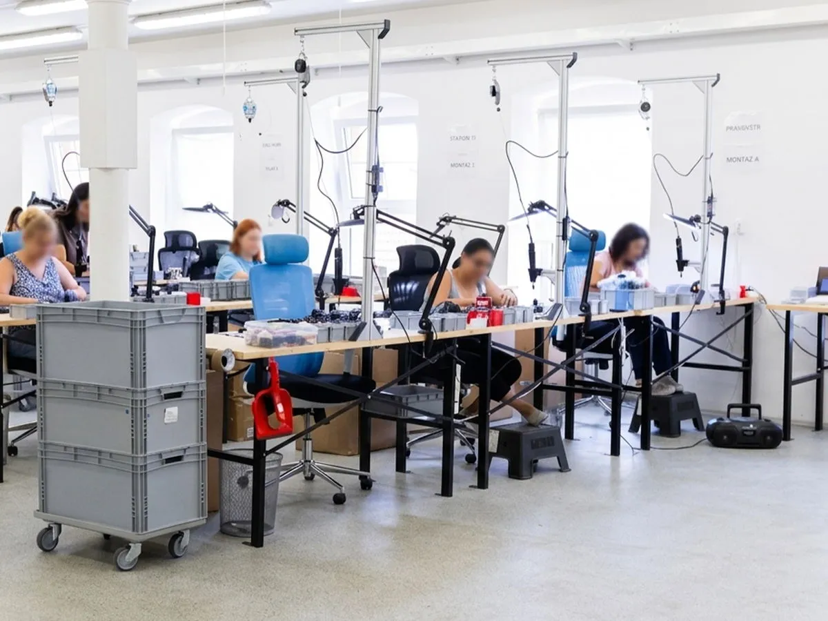 Reihen von Montagetischen mit Schraubern an Federzügen und Lupenleuchten auf der Fertigungsfläche von HARDWARIO Studio, daneben Handbestückungsplätze und die 3D-Druckfarm